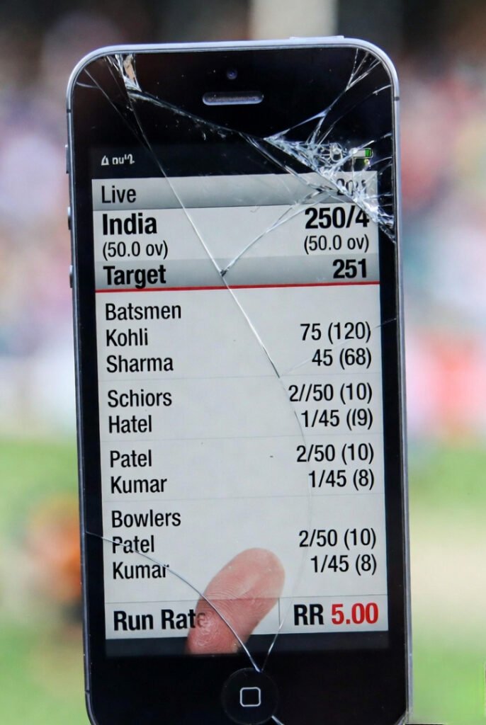 Cracked screen close-up: cricket live updates, thumbprint hiding run rate, unsteady joyful capture.