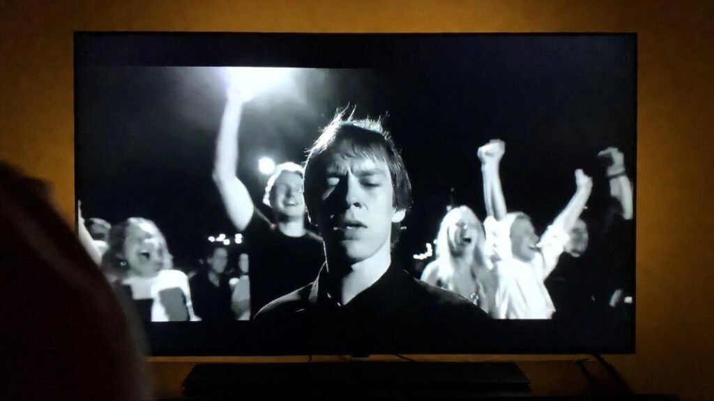 TV screen frozen mid-celebration, your tired and pissed-off reflection visible, slight motion blur from frantically mashing the capture button.