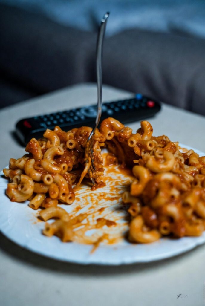 Half-eaten chili mac on a plate, fork stuck mid-bite, TV remote nearby during rain delay.