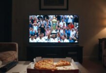 Cricket Leagues Highlights: Most Dramatic Finals Ever Personal watch setup – TV frozen on a cricket final trophy lift, open pizza box and remote in the foreground, typical messy American living room scene."