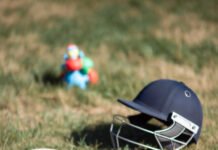 Cricket Gear Trends: Latest Equipment in Modern Cricket "Close-up from ground level: cricket bat, ball, and helmet haphazardly arranged on lawn with a bright plastic toy figure nearby."